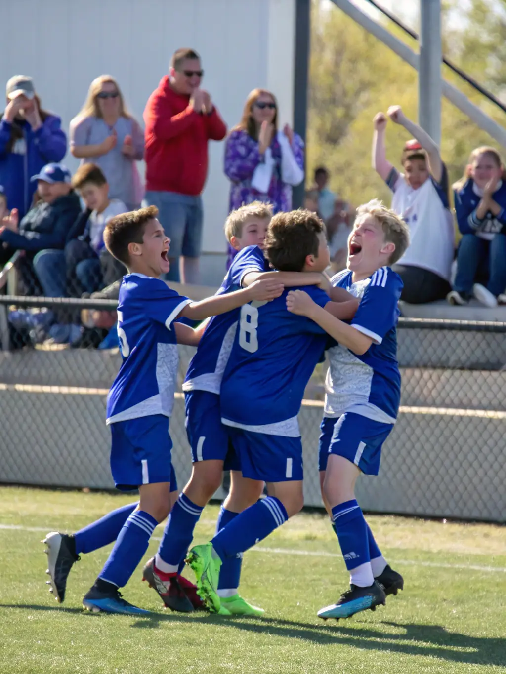 Action shot of a youth soccer team in UNION SPORTIVE TOUCYCOISE jerseys celebrating a goal during a sunny afternoon game, showcasing teamwork and sportsmanship.